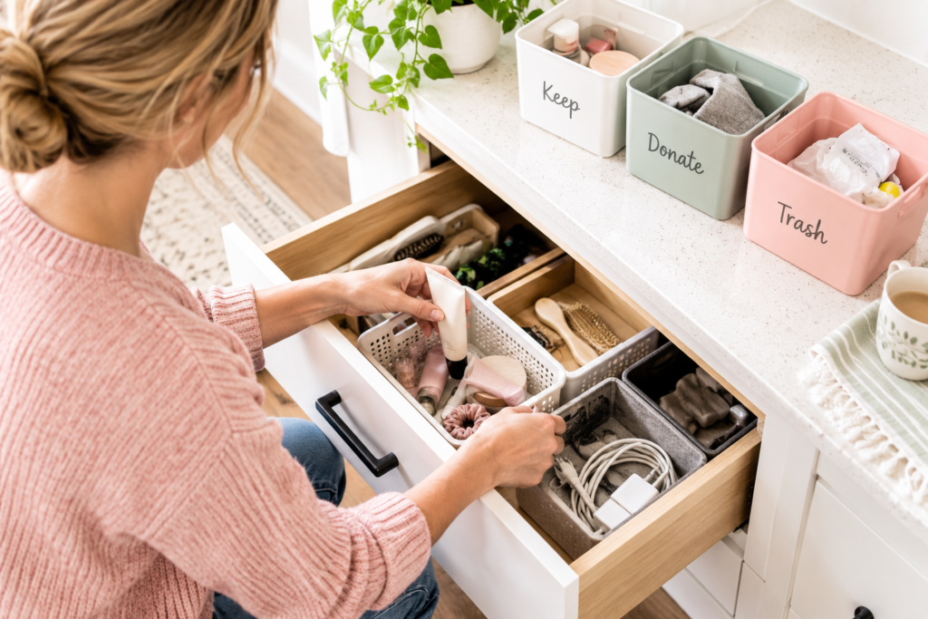 Woman sorting a drawer using keep, donate, and trash bins while decluttering